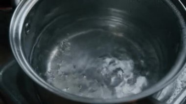Yakın çekim yüksek açılı kaynamış su portatif fırının üzerindeki paslanmaz çelik tencerede dönüyor.