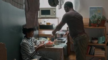 Oğlu mutfakta oturmuş gazete okurken zavallı Afrikalı Amerikalı adam bardağa kaynar su dökerken...