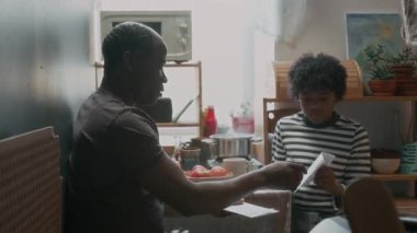 Zavallı Afrikalı Amerikalı, oğluyla vadesi geçmiş faturalar hakkında konuşuyor. Küçük bir mutfakta birlikte oturuyor.