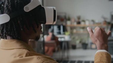 VR kulaklık takan siyah bir adam, havadaki görünmez etkileşimli elementleri aşırıyor, büyük teknoloji şirketinin ofisinde sanal gerçeklik uygulamasını test ediyor.