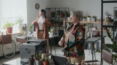 Protez kollu genç bir kadın iş gününün ortasında fabrikalarla dolu bir ofiste kadın meslektaşlarıyla esneme egzersizleri yapıyor.