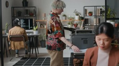 Protez elli genç bir kadın belgeyi taramak için yazıcı kullanırken, çok ırklı meslektaşları da rahat açık planlı ofislerdeki masalarda tablet kullanıyor ve kodluyorlar.