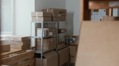 Farklı boyutlarda karton kutularla dolu bir depo, metal raf ünitesi ve beyaz duvarda dokümanları gösteren bir pim tahtası yok.