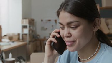 İş günü depoda müşteriyle telefon görüşmesi yapan Latin kökenli genç bir kadının yakın plan görüntüsü.