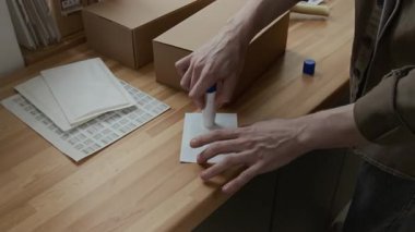 Bilinmeyen bir depo çalışanının yakın plan fotoğrafı. Nakliye etiketine yapıştırıp küçük bir karton kutuya yapıştırıyor.