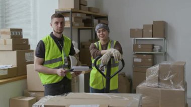 Ciddi bir milenyum erkeğinin portresi ve sayısız kutuyla dolu depoda kameraya yansıtıcı yelek giyen gülümseyen Z jenerasyonundan bir kız.