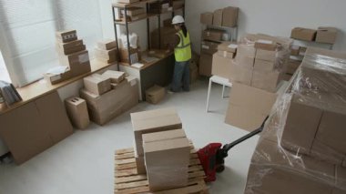 Erkek depo görevlisinin el arabası ile iki büyük kutu çekerken yüksek açılı görüntüsü, tarayıcı kullanarak barkod okuyan bir kadın.