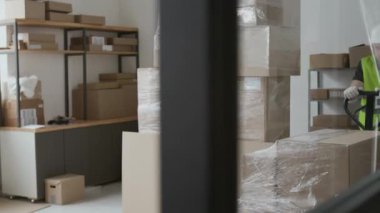 Erkek depo çalışanı, kasketli, yansıtıcı yelek ve eldivenli iş günü ağır kutularla manuel forklift kullanıyor.