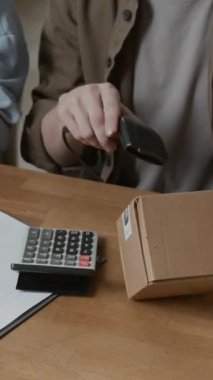 Bilinmeyen erkek depolama yöneticisinin küçük kutuda barkodu tararken çalışma masasında meslektaşıyla birlikte dikey yakın görüntüsü