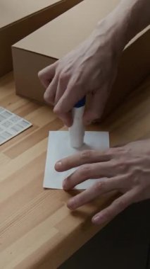 İş yerindeki karton kutuya nakliye etiketi yapıştırmak için yapıştırıcı kullanan tanınmayan bir gencin elleri dikey yakın plan görüntüsü