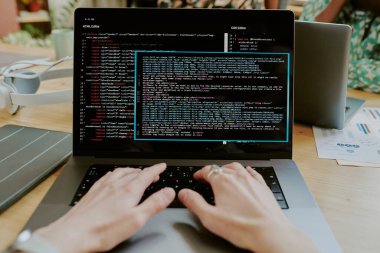 Ofisteki dizüstü bilgisayardaki kod satırlarını düzenleyen tanımlanamayan kadın elleri.