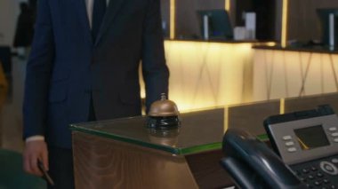 Girişteki otel resepsiyonunda servis zilini çalan takım elbiseli misafirin yakın görüntüsü