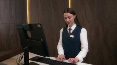 Kontrol masasındaki bilgisayarda daktilo eden genç bir bayan resepsiyonistin portresi, sonra da otelde çalışırken gülümseyerek kameraya poz vermek.