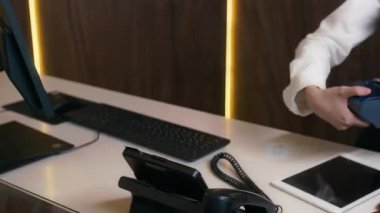 Otelin resepsiyonistinin kontrol sırasında tuttuğu satış noktasında kredi kartıyla ödeme yapan misafirin el görüntüsünü kapatın.
