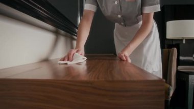 Otel odasının manzarasını kapatın. Üniformalı görevli temizlik sırasında ahşap masayı kumaşla dikkatlice siliyor.