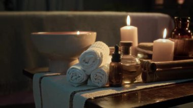 Yuvarlanan havlular, kase, yağ şişeleri, yanan mumlar ve kaplıcadaki ahşap masaya dizilmiş bambu silindirler.