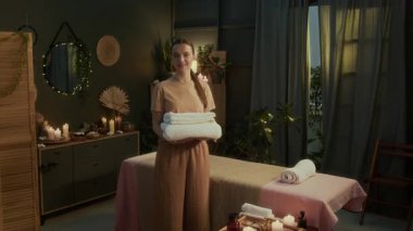 Profesyonel masözün portre fotoğrafı. Kameraya bakıyor ve gülümsüyor. Elinde temiz havlular, otantik kaplıca odasında duruyor.