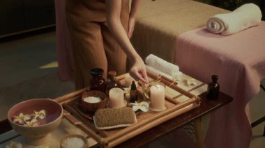 Tanımlanamayan masözün yüksek açılı görüntüsü. Bambu tepsisi üzerinde mum yakmak, spa 'da masaj seansına hazırlanmak.