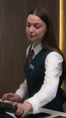 Kadın otel resepsiyonistinin bilgisayarda yazarken dikey görüntüsü, sonra da resepsiyondaki telefona cevap vermesi.