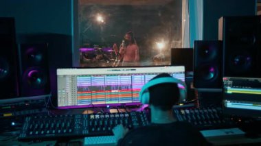 Çocuk bandosunun yeni şarkısını kaydederken kontrol odasında profesyonel ses karıştırıcı kullanan kulaklıklı genç erkek müzik yapımcısının arka görüntüsü