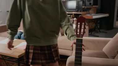 Kızıl saçlı ergen müzisyen akustik gitar çalıyor, koltuğa oturuyor ve stüdyoda çocuk grubu provasında enstrüman çalmaya başlıyor.