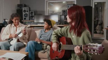 Beyaz saçlı genç gitarist Afrikalı Amerikalı ergen kemancı ve şarkıcı ile müzik stüdyosunda prova yapıyor.