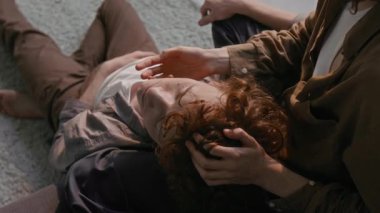 Kızıl saçlı adam tanınmayan kız arkadaşının kucağında başını dinlendiriyor, yanağını okşuyor ve yerde oturuyor.