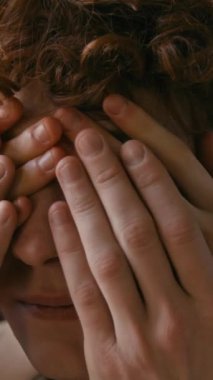 Erkek arkadaşının gözlerini kapayan, nazikçe ellerini öpen, tanınmayan bir kadının dikey yakın çekimi.