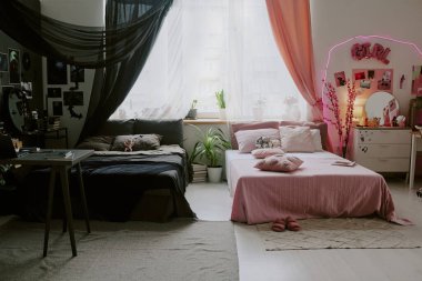 Kız kardeşlere geniş bir oda, odanın bir tarafı siyah mobilyalar ve gizemli ve ürkütücü posterlerle süslenmiş, diğeri de barbiecore tarzını gösteriyor.