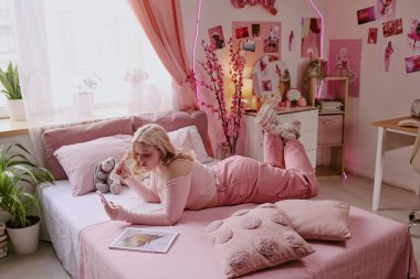 Sosyal medyayı akıllı telefondan kontrol ederken yatakta uzanan genç blogcu, tamamen pembe giyinmişti.