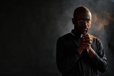 Siyah cübbeli Afrikalı rahip elinde altın haçla odada sessizce tütsü dumanıyla dua ederken...