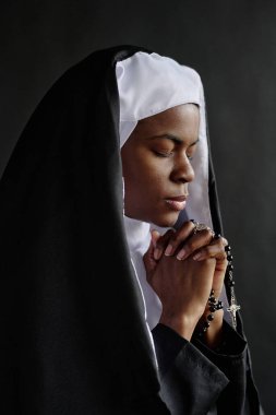 Güzel Afrikalı Amerikalı rahibenin elinde tespihle sessizce dua ettiği dikey çekim.