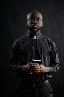 Genç Afrikalı Amerikalı kilise liderinin dikey portresi. Elinde İncil ve tespihle fotoğraf çektirirken.
