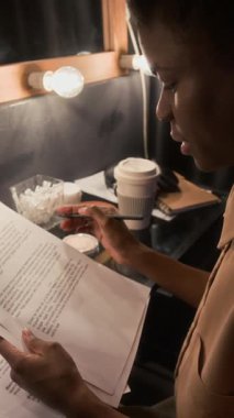 Afro-Amerikalı bir kadının kağıt senaryoya not alıp soyunma odasındaki masada oturduğu dikey yakın çekim.