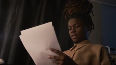 Düşük açılı çekimde Afrikalı Amerikalı kadın stand-up gösterisini loş ışıklı soyunma odasında yüksek sesle prova ediyor.