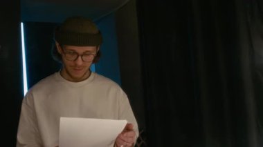 Gözlüklü genç adam aynada kendine bakıyor, soyunma odasındaki stand-up gösterisine hazırlanıyor.