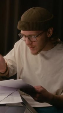 Gözlüklü genç adamın kağıda yazı yazarken, loş aydınlatılmış soyunma odasında, sahneye çıkmaya hazırlanırken dikey bir fotoğrafı.