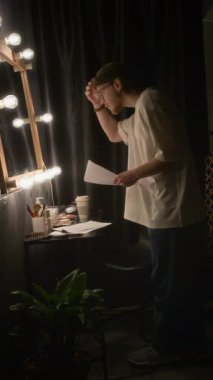 Adamın aynada kendine baktığı ve soyunma odasında performans senaryosunu tekrar okuduğu dikey bir fotoğraf.