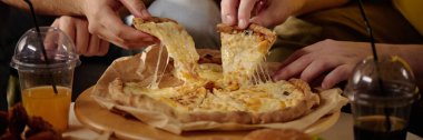Bir grup arkadaş peynirli pizzayı yapışkan erimiş peynirle ve ferahlatıcı içeceklerle paylaşıp eğleniyorlar. Birlikte geçirdikleri bir anı yakalıyorlar ve mutfaktan haz alıyorlar.