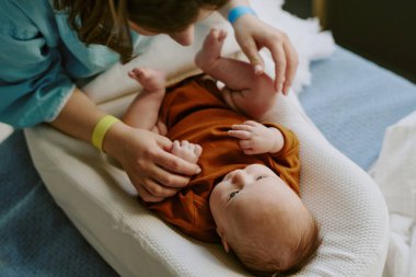 Anne ve baba yastıklı bir yüzeyde yatan yeni doğmuş bebekle karşılaşır. Yumuşak yatak ve güvenli atmosfer ile desteklenen, beslenme etkileşimini gösteren sahne