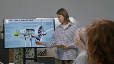 Rüzgâr türbiniyle ilgili grup alkış sahnesinin yavaş çekimi, geniş ekranda gösteriliyor, ev ve rüzgar türbini modelleriyle birlikte.