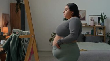 Latin kadın evde antrenmandan önce spor kıyafetlerini giyerken aynanın karşısında duruyor.