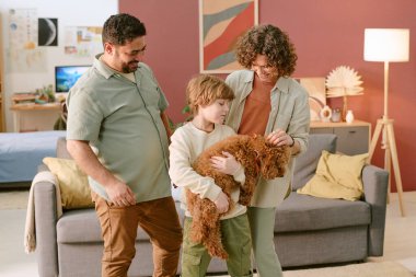 Beyaz çocuk küçük bir köpek tutarken orta yaşlı beyaz kadın hayvan besliyor ve orta yaşlı siyahi adam gülümsüyor, aile ilk evcil hayvanla evde iletişim kuruyor.