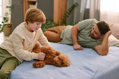 Orta yaşlı Orta Doğulu bir adam izlerken ve gülümserken beyaz çocuk yatakta küçük kahverengi bir köpeği okşuyor. Ev tecrübesi ve aile bağlarının ilk evcil hayvanını yakalıyor.