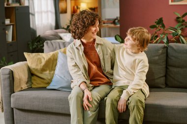 Kafkasyalı orta yaşlı bir kadın kanepesinde oturuyor. Yanında oturan beyaz çocuğa gülümsüyor. İkisi de birbirine bakıyor.