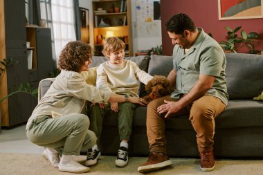 Kafkasyalı kadın, beyaz çocuk ve Orta Doğulu adam koltukta oturuyor. Evdeki ilk evcil hayvan olarak kıvırcık saçlı yavru köpeği tanıtıyorlar.