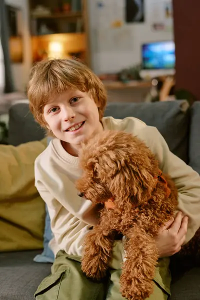 Evdeki kanepede küçük kahverengi bir kanişi tutarken gülümseyen beyaz çocuk portresi, aile ortamında ilk evcil hayvan deneyimi sırasında heyecan ve şefkat gösteriyordu.