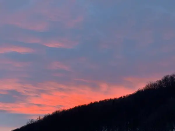 暗い山の森の上の曇った空の美しいオレンジの日没 ロイヤリティフリーのストック写真