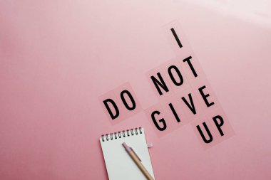 Küçük not defteri ve kalemle pembe arkaplandaki mesajdan vazgeçmem. Motivasyonal ilham verici modern mesaj kavramı.