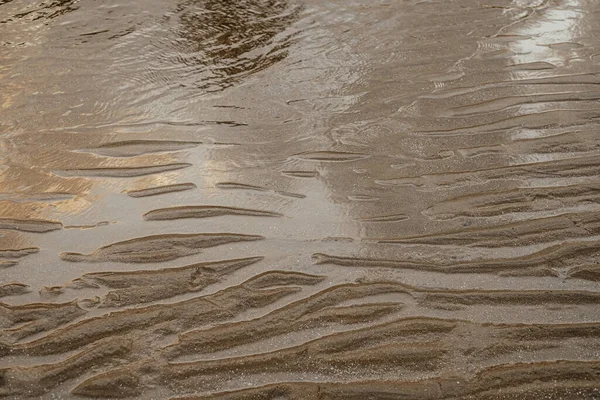 Waves of sand. Textured sand with reflection in water. Texture of sand when a tide is low.